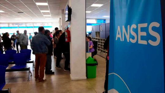 Calendario de pagos de ANSES sobre un escritorio con un teléfono celular mostrando la aplicación Mi ANSES.