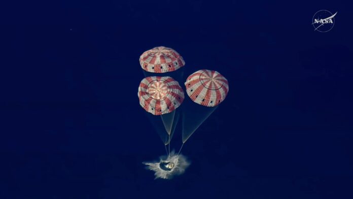 La cápsula Orion de la NASA flota en el Océano Pacífico tras su amerizaje exitoso, con paracaídas desplegados.