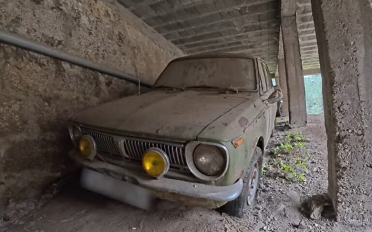 Interior de un galpón abandonado con varios autos clásicos japoneses cubiertos de polvo.