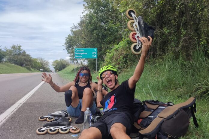 Maure y Oscar, los Parceros Mochileros, sentados en la ruta con sus patines y mochilas
