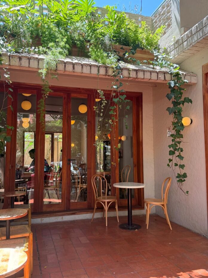 Interior del café Zulu Haus en La Lucila, con pérgola de flores y mesas de madera