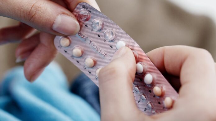 Mujer sosteniendo un blister de pastillas anticonceptivas junto a un plato de comida
