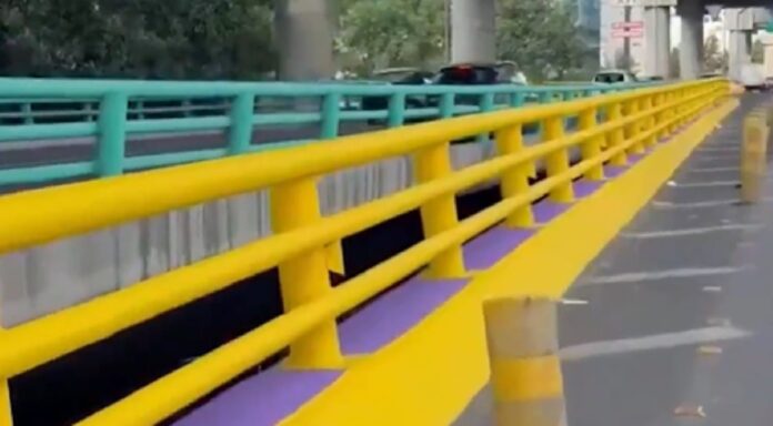 Trabajadores repintando de amarillo una barrera vial elevada en la Ciudad de México durante la noche