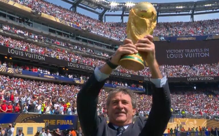 Mario Alberto Kempes y Andrés Iniesta sosteniendo la Copa del Mundo en el campo del MetLife Stadium